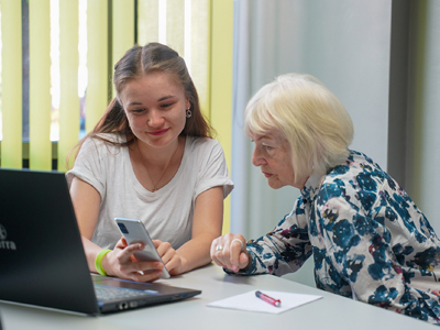 Schülerin zeigt Seniorin etwas auf dem Smartphone 