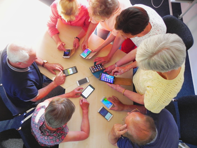 Ältere Menschen sitzen am Tisch und schauen auf ihre Telefone, die auf dem Tisch liegen