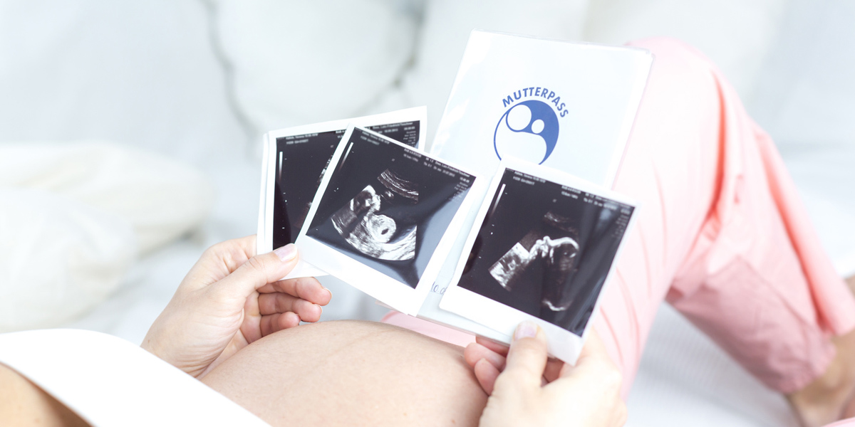 Schwangere Frau betrachtet Ultraschallbilder und hält Mutterpass, Foto: © mmphoto / Fotolia